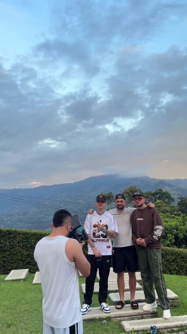 Tres artistas de FAMA i. posando frente a cámara al atardecer, con las montañas de Medellín detrás.